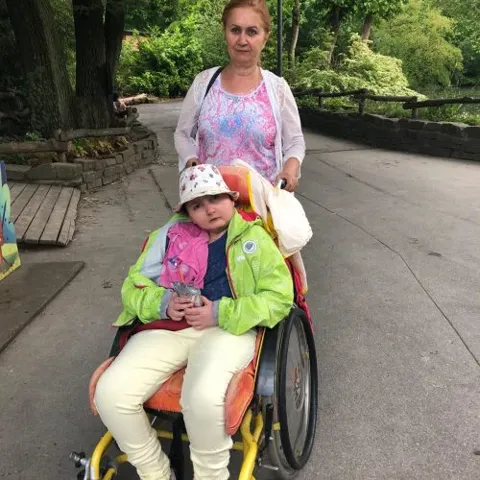 Frau schiebt ein Kind im Rollstuhl auf einem Weg durch den Park
